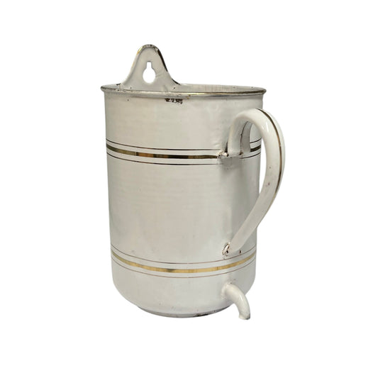 A vintage metal jug with a white enamel body, decorated with two thin gold stripes, a white handle, and a small pouring spout at the bottom.