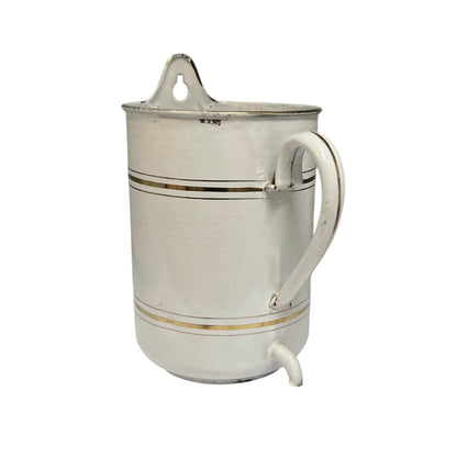 A vintage metal jug with a white enamel body, decorated with two thin gold stripes, a white handle, and a small pouring spout at the bottom.