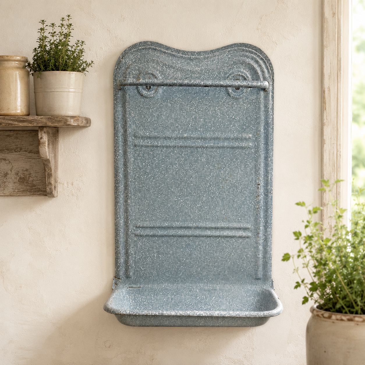 A speckled slate blue wall-mounted utensil rack with a curved top and integrated tray, shown mounted on a textured cream wall with potted plants nearby.