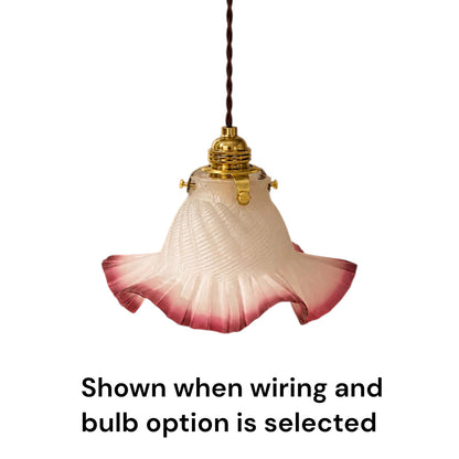 A vintage-style pendant light with a fluted glass shade that fades from off-white to pink at the bottom, suspended by a dark brown cord with gold-toned metal hardware. Text below reads, 'Shown when wiring and bulb option is selected' on a plain white background.