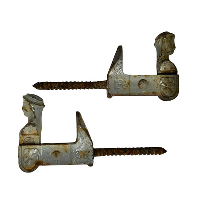 Two vintage metal shutter dogs with threaded screws, showing weathered silver and rusted brown patina on a plain white background.