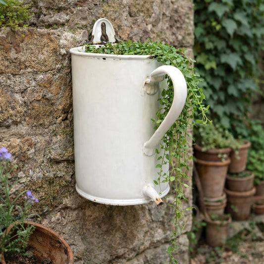 White metal wall-mounted planter with greenery against a stone wall