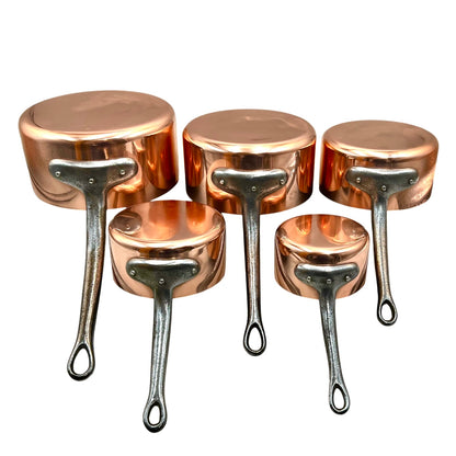 Five copper saucepans in different sizes with silver metal handles, arranged on a plain white background.