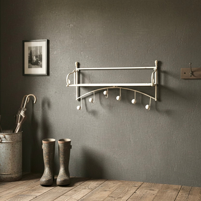 Wall-mounted coat rack with hooks on a gray wall, next to boots and an umbrella.