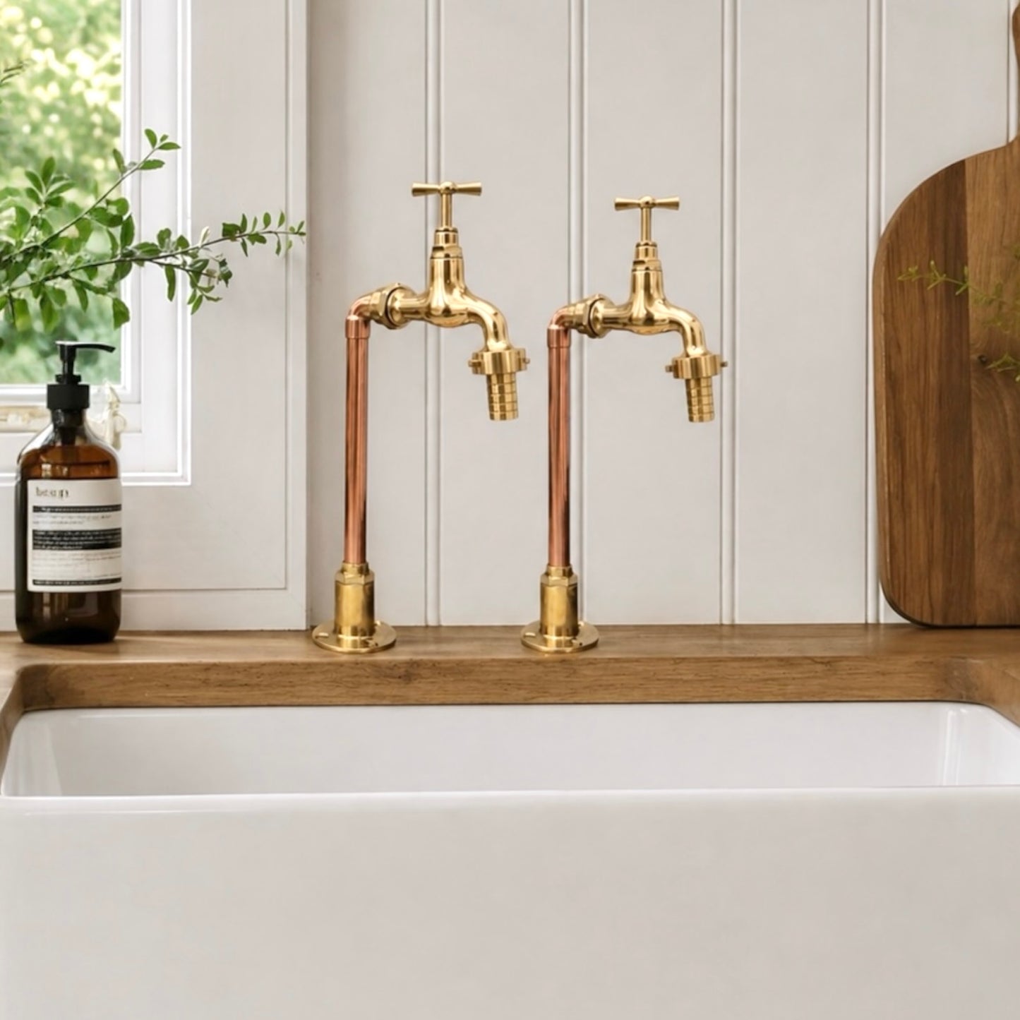 A pair of gold faucets sit on a wooden countertop beside a white sink.