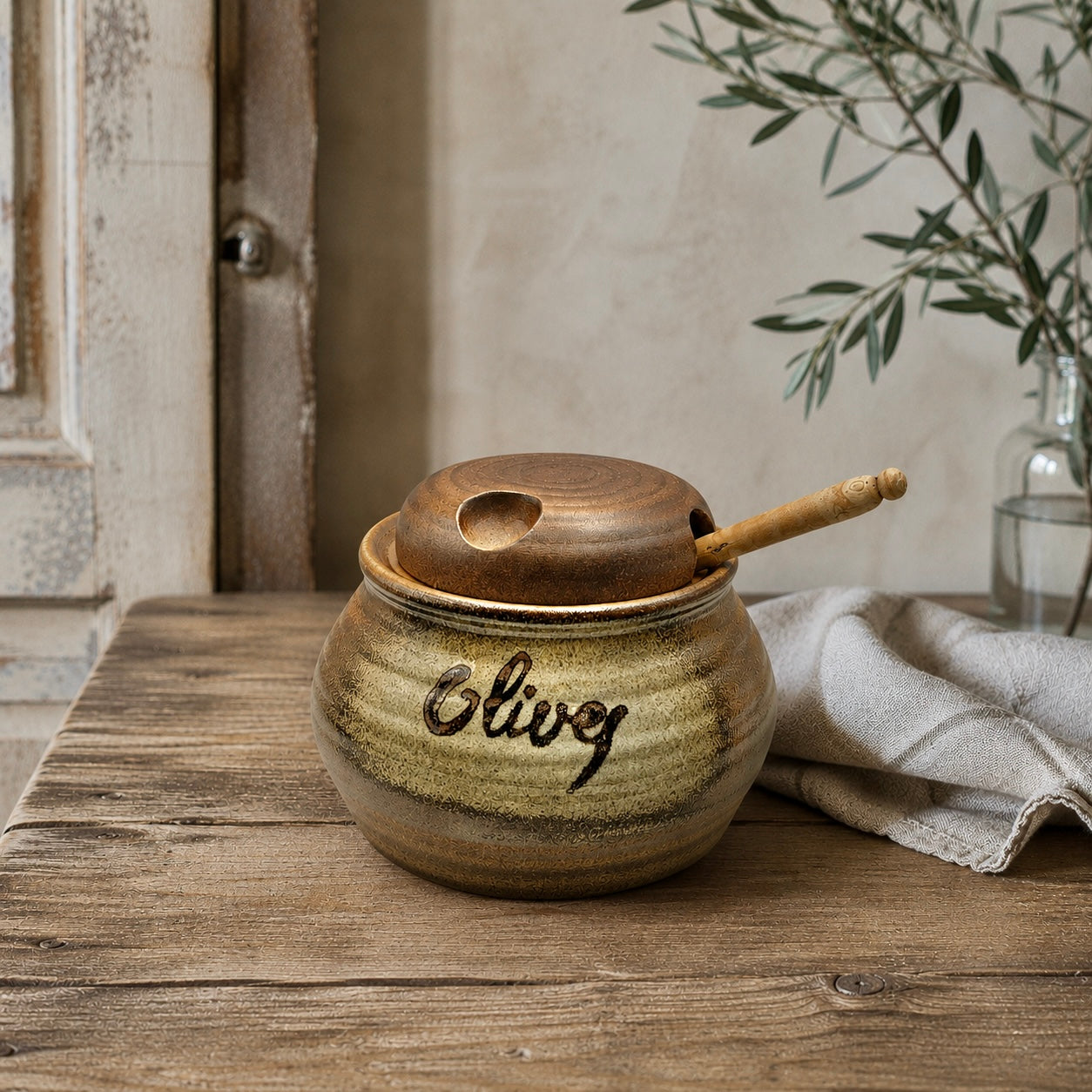 A ceramic jar with a lid and wooden handle sits on a wooden surface, adorned with the word 'Olive', perfect for adding charm to a farmhouse or country cottage.