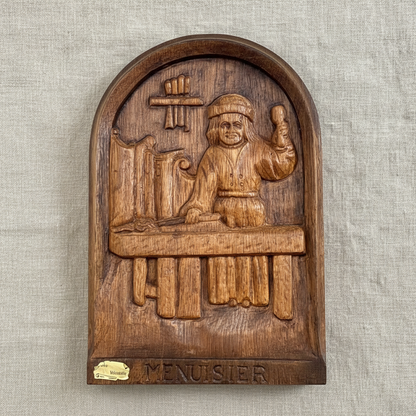 Wooden plaque with a carved figure and 'Menuisier' text on a textured beige background