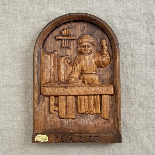 Wooden plaque with a carved figure and 'Menuisier' text on a textured beige background