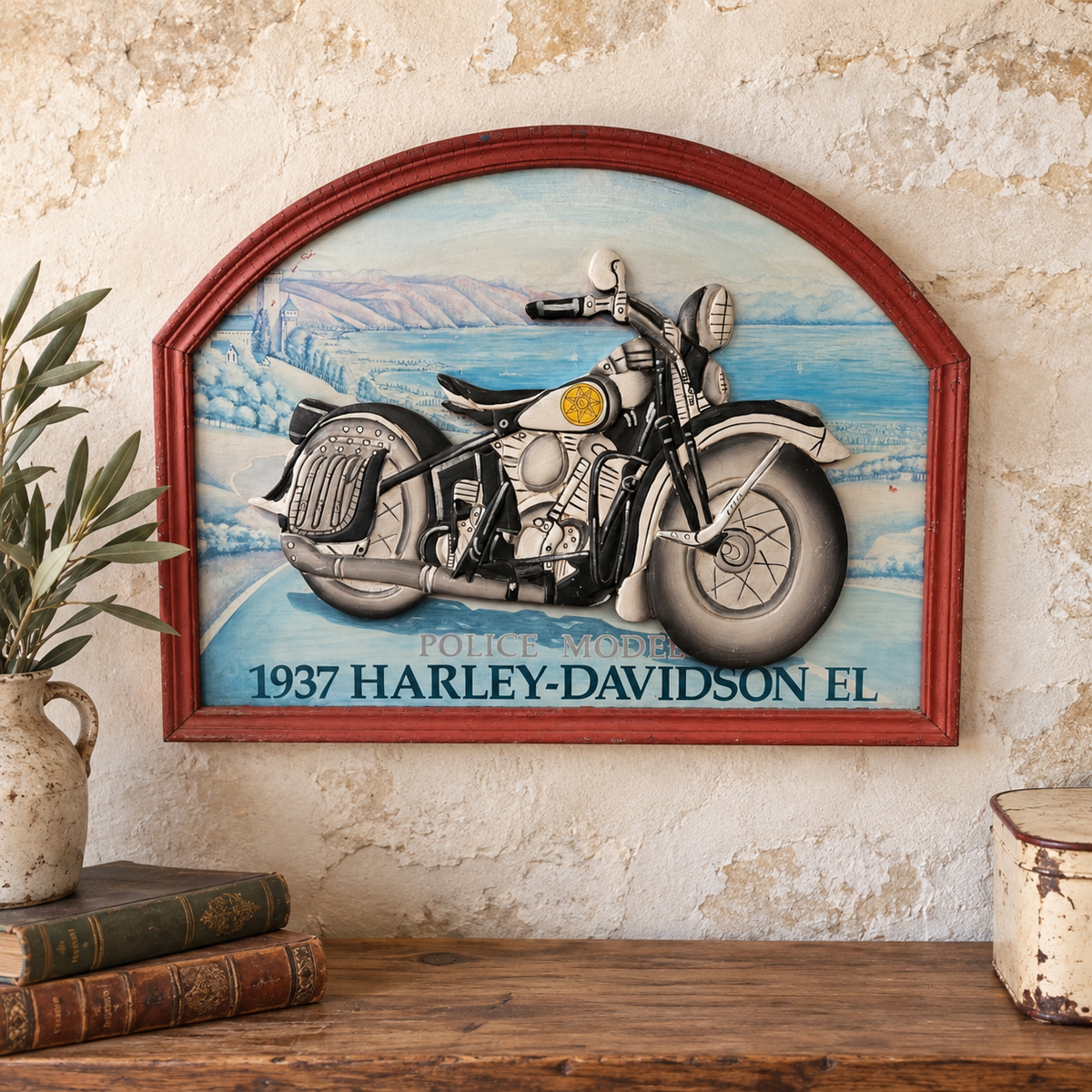 A framed wall art piece featuring a vintage 1937 Harley-Davidson motorcycle illustration, displayed on a rustic wall above a wooden shelf with books and a plant.