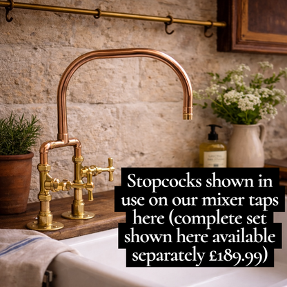 Copper mixer tap with stopcocks on a kitchen counter, featuring a stone wall background.