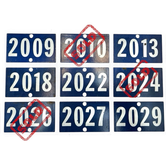 Nine French enamel vintage blue and white door numbers on a white background ranging from 2009 - 2029