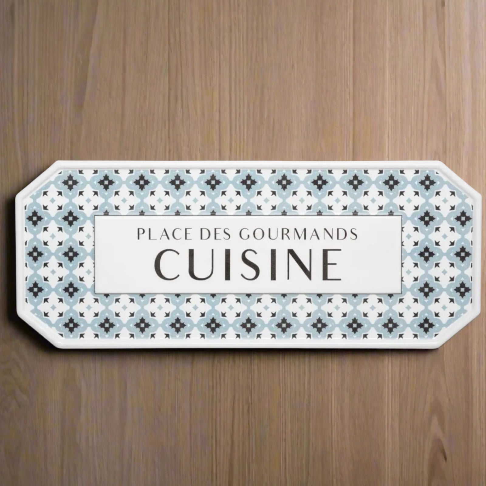 Decorative sign with patterned border and text on a wooden surface