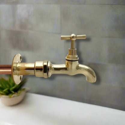 Brass wall mounted tap on a grey background