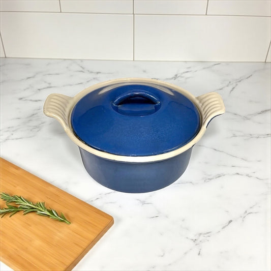 Blue ceramic cast iron casserole dish with beige handles on a marble countertop.