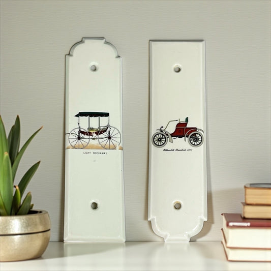 Two decorative porcelain door push plates with vintage car illustrations on a light grey background.