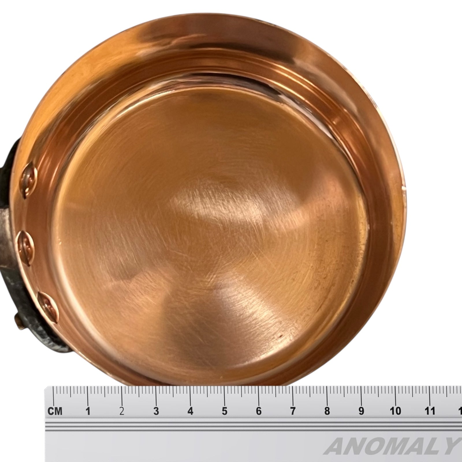 Copper pan with a ruler for scale on a white background