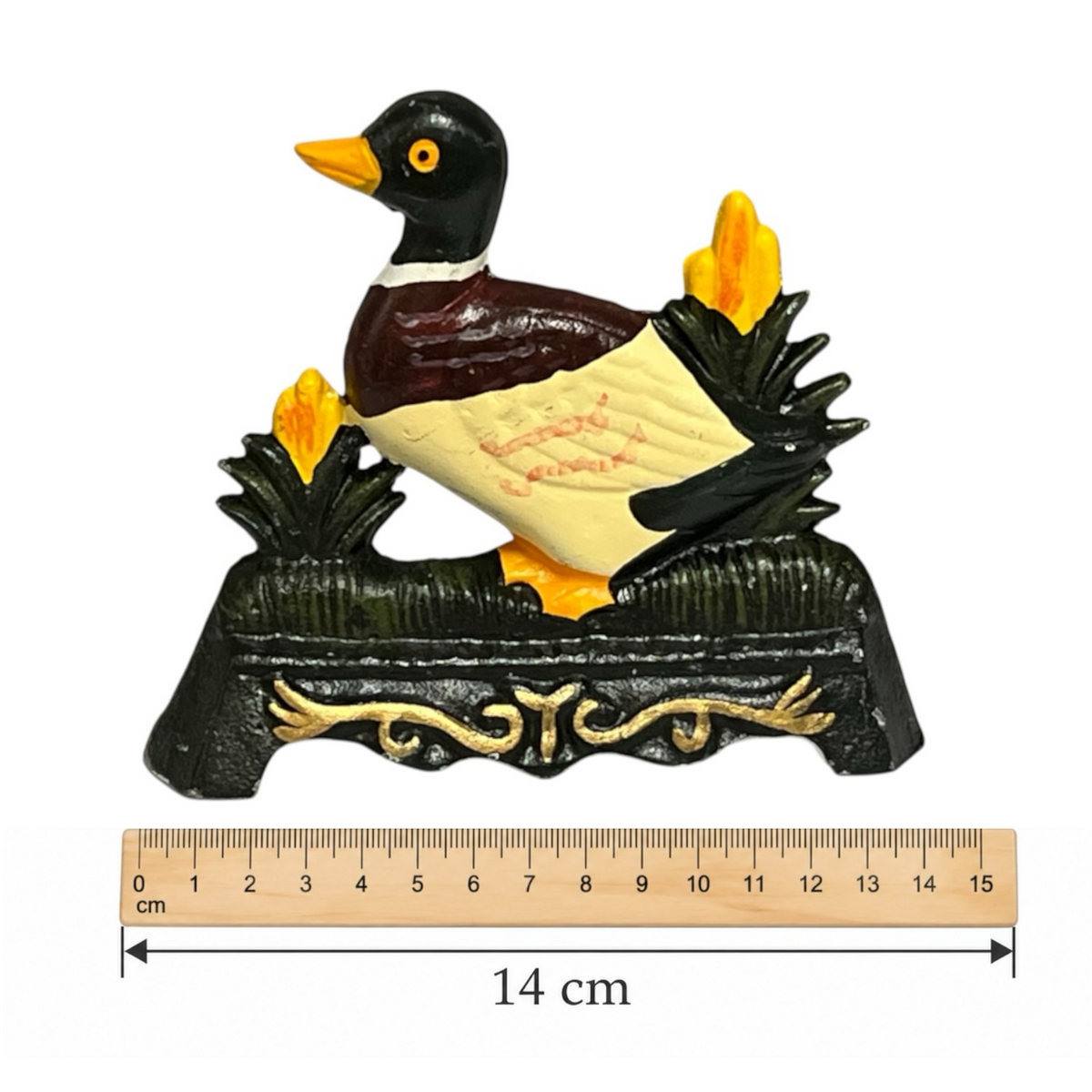 A decorative duck figurine with a black head and neck, dark brown chest, cream body, and yellow beak and feet, perched on a dark base with gold scrollwork and yellow reeds. A wooden ruler at the bottom shows the item is 14 cm long.