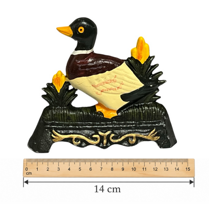 A decorative duck figurine with a black head and neck, dark brown chest, cream body, and yellow beak and feet, perched on a dark base with gold scrollwork and yellow reeds. A wooden ruler at the bottom shows the item is 14 cm long.