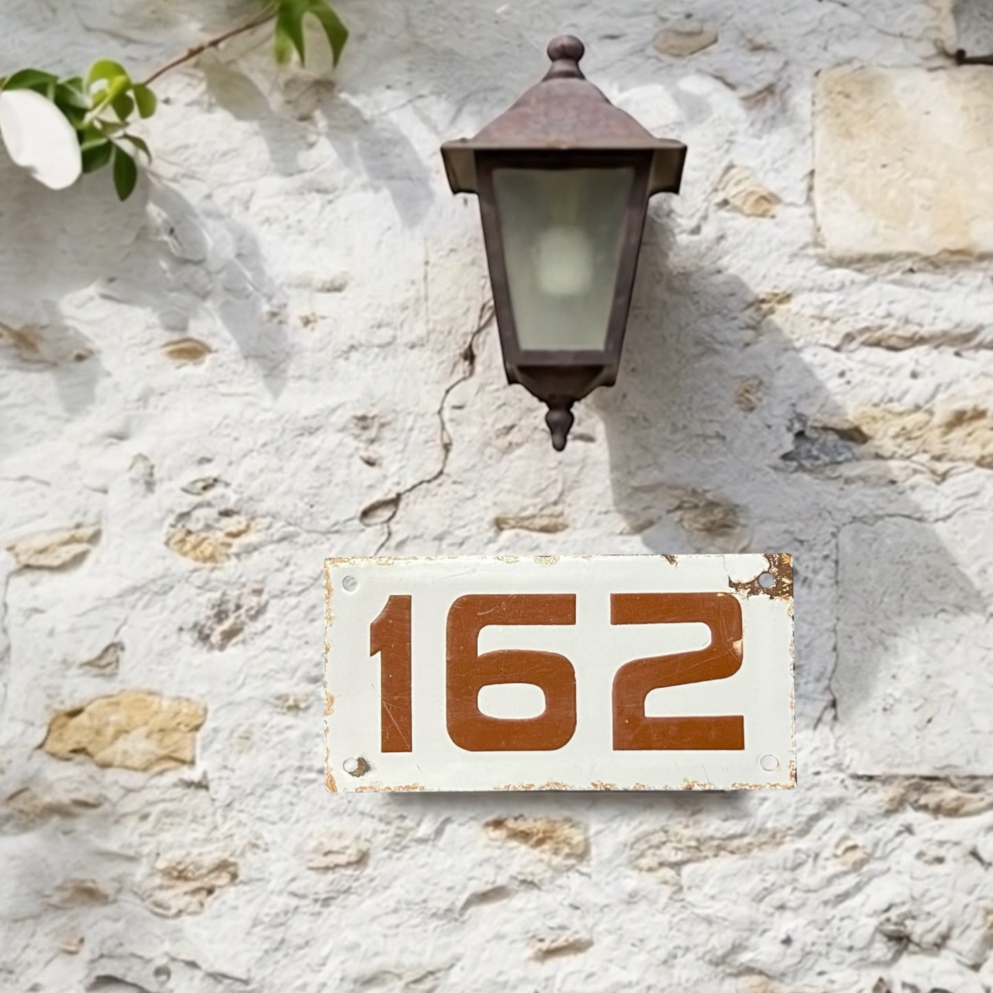 House number '162' on a stone wall with a vintage-style lamp.