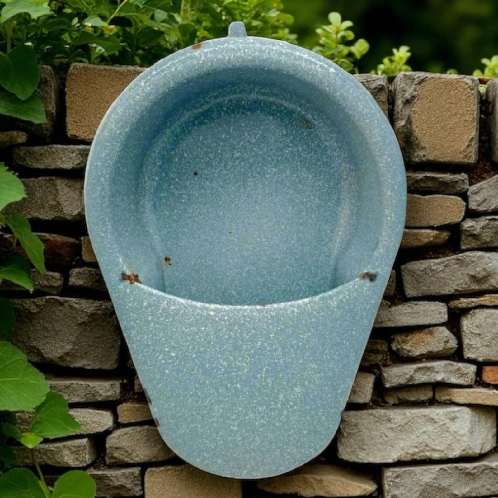 Blue ceramic planter attached to a stone wall with greenery in the background
