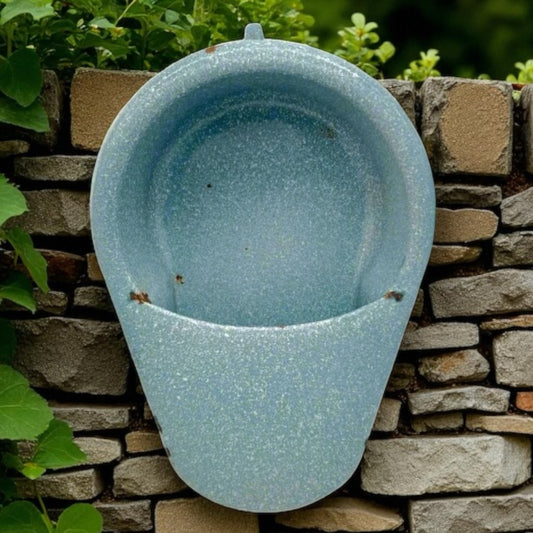 Blue ceramic planter attached to a stone wall with greenery in the background