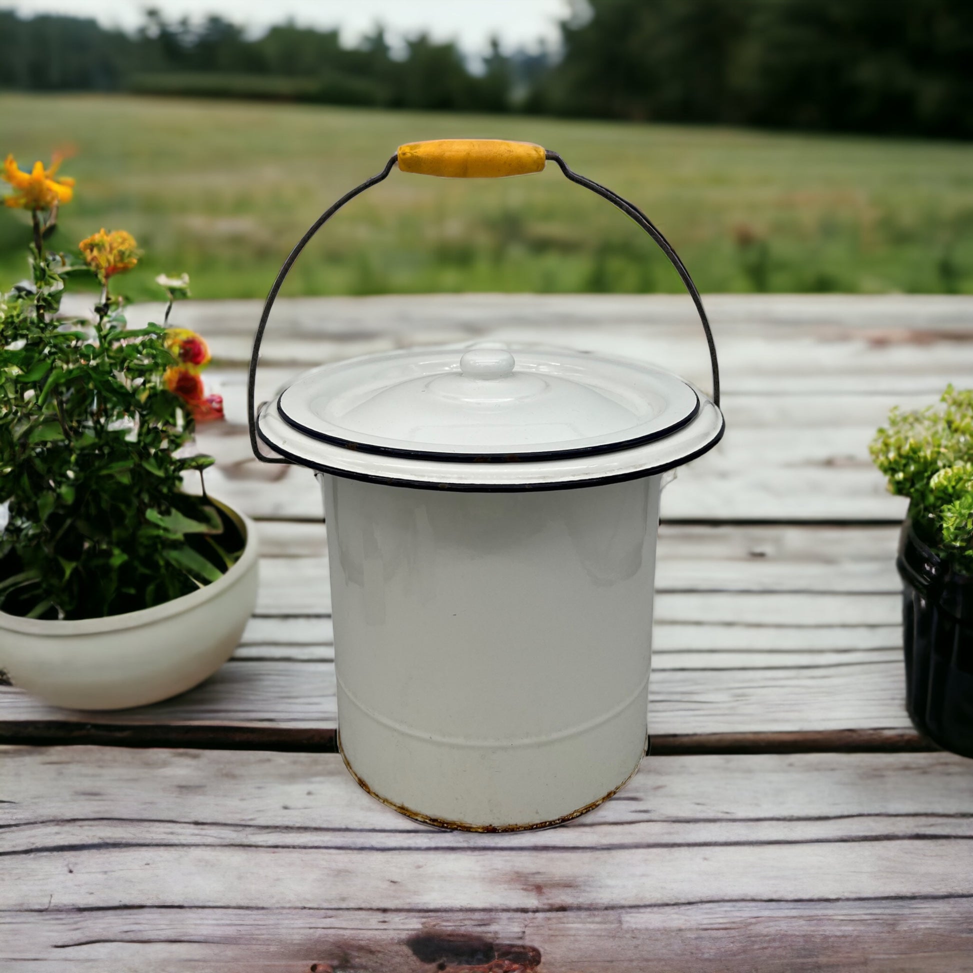 image French vintage enamel lidded bucket on a wooden table with a garden in the background