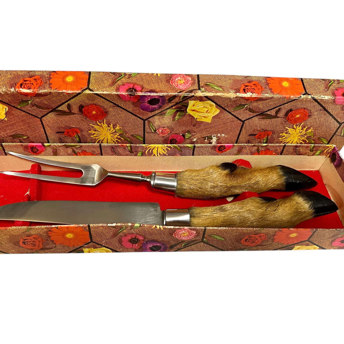 A two-piece serving utensil set inside its floral-patterned gift box. The set includes a decorative serving fork and a matching serving knife, both featuring handles made of natural animal fur with black-tipped hooves and silver metal bolsters.