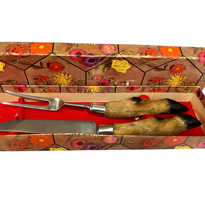 A two-piece serving utensil set inside its floral-patterned gift box. The set includes a decorative serving fork and a matching serving knife, both featuring handles made of natural animal fur with black-tipped hooves and silver metal bolsters.