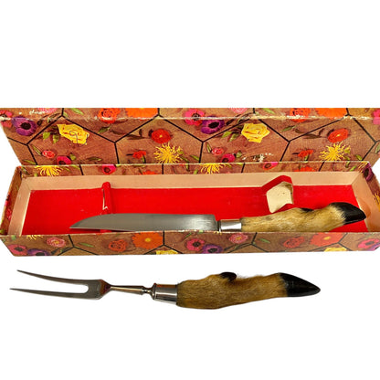 A two-piece serving utensil set consisting of a knife and a two-pronged fork, both featuring natural animal fur handles with black tips, displayed with their vintage floral-patterned presentation box on a white background.