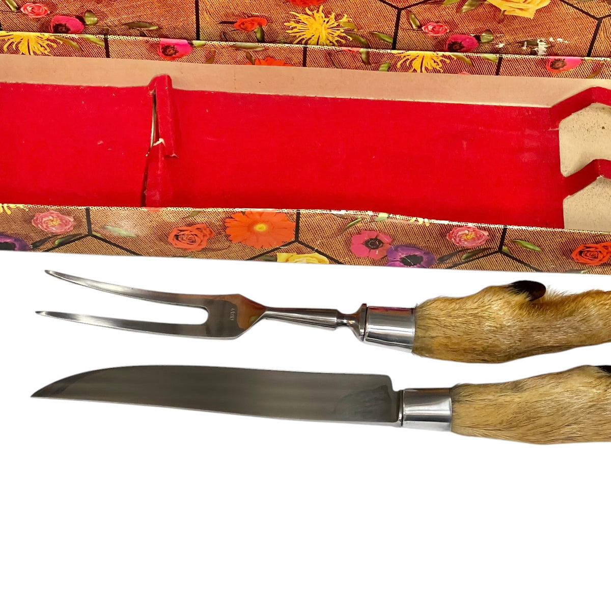 A two-piece serving utensil set featuring a stainless steel carving fork and knife with natural animal hide handles, displayed alongside a red velvet-lined box with a floral-patterned lid on a white background.