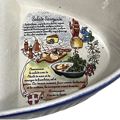 Close-up of the inside of a ceramic bowl or dish featuring a printed French recipe illustration for Salade Savoyarde, with illustrated ingredients, text, and a blue rim visible along the edge.