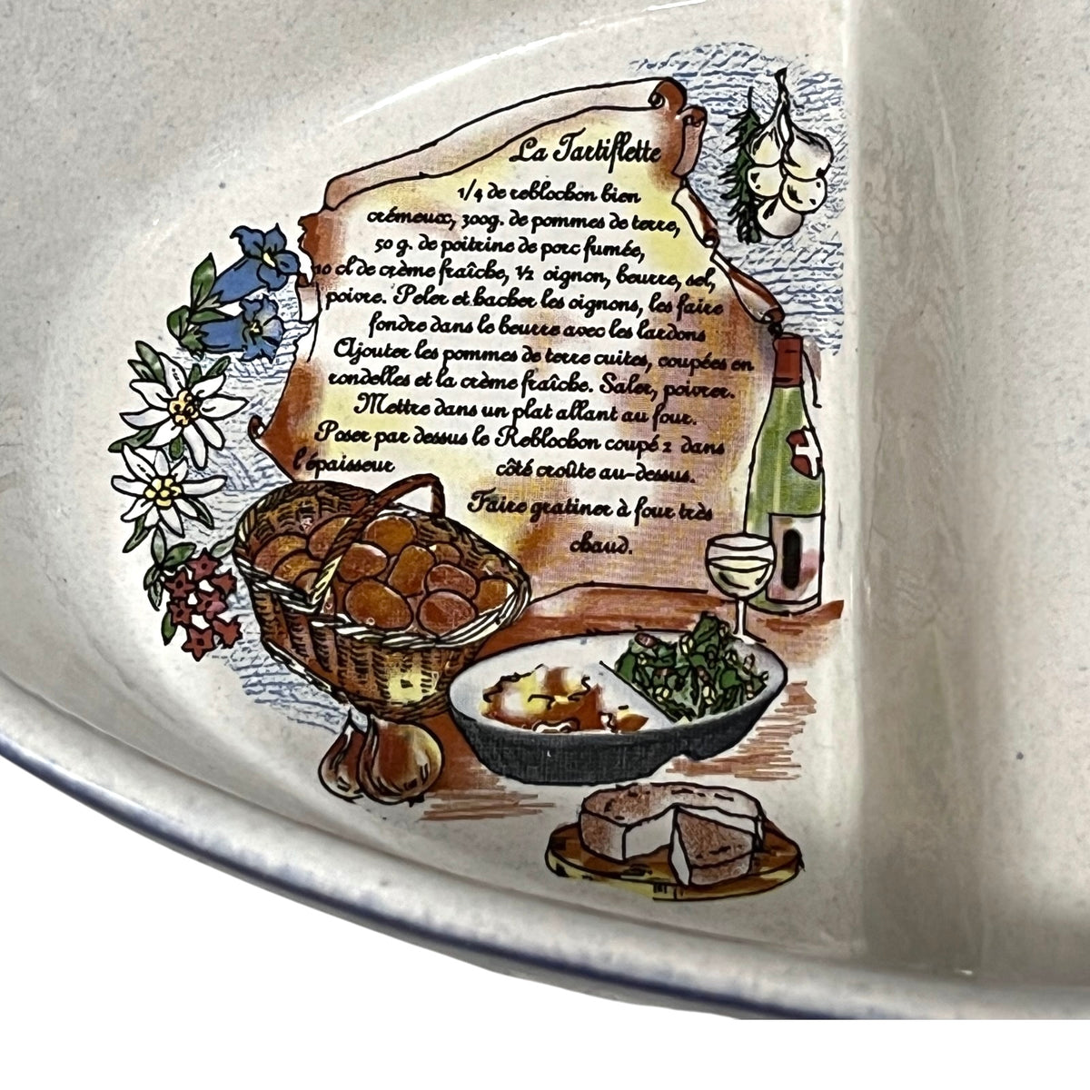 Close-up of a ceramic plate or bowl featuring a detailed hand-painted illustration of French recipe. The artwork includes a parchment-style recipe label with French text, a basket of tarts, a bowl of sauce and greens, garlic, a bottle, and a wine glass, all on a warm off-white ceramic background.