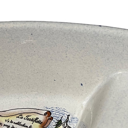 Close-up of a speckled off-white ceramic dish, showing part of a printed illustration and text near the bottom edge.
