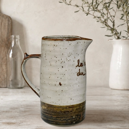 Ceramic pitcher with speckled design and text on a wooden surface