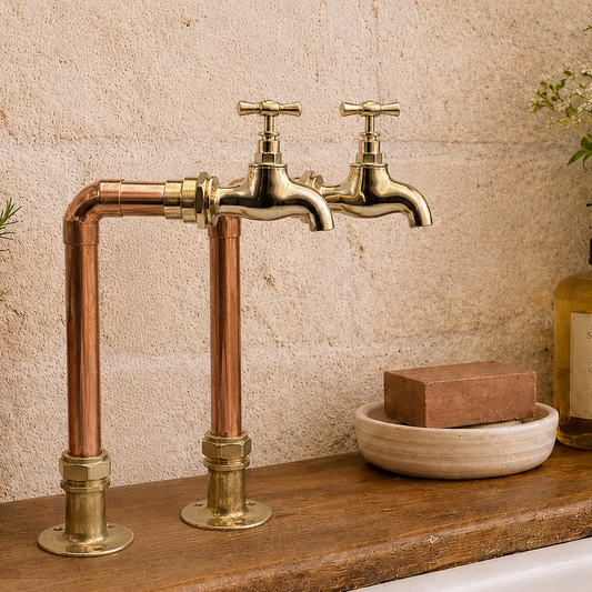 Pair of copper and brass kitchen pillar tall taps displayed on wooden counter over a Belfast sink 