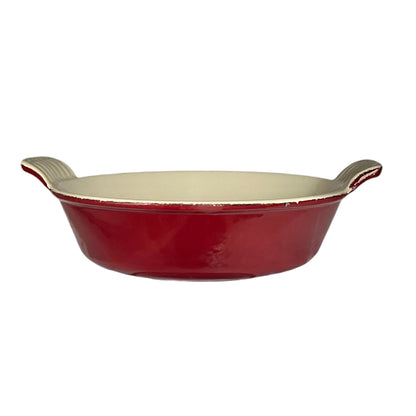 A red round ceramic baking dish with a cream-coloured interior and textured handles, shown against a plain white background.