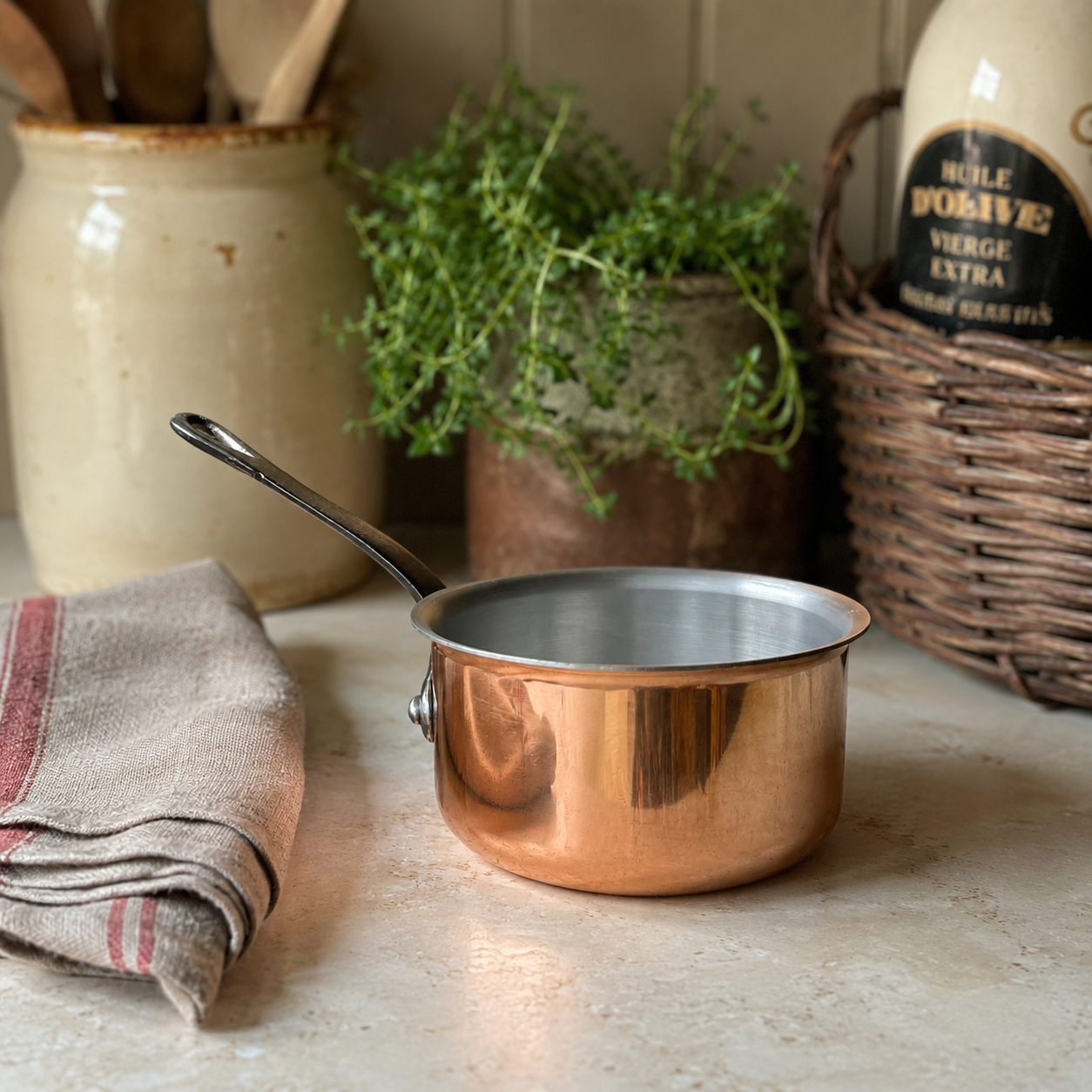 French copper mini pan on a kitchen counter with herbs and pots in the background 