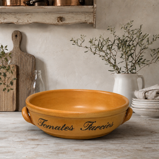 Stoneware bowl with handles and text on a wooden surface, rustic kitchen setting.