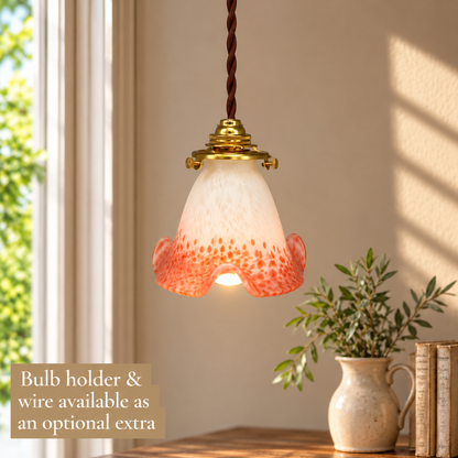 Vintage French pendant lampshade in mottled white glass with coral pink and orange speckled detailing and a decorative scalloped, flower-shaped rim. Measuring 12 cm high and 13 cm in diameter, the illuminated glass shade is displayed with a polished brass bulb holder and brown twisted fabric wiring, hanging in a softly lit French country interior. A neutral beige wall, sunlit window, rustic wooden table, ceramic jug with greenery and vintage books create a simple, elegant background. A beige text box in the