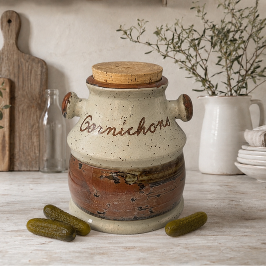 Vintage French cornichon pickle jar with cork lid on a rustic farmhouse kitchen countertop, styled with small pickles, wooden boards and French country kitchen decor.