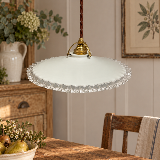 A vintage-style pendant light with a white scalloped glass shade and a gold brass ceiling mount, hanging in a warm, rustic dining room setting.