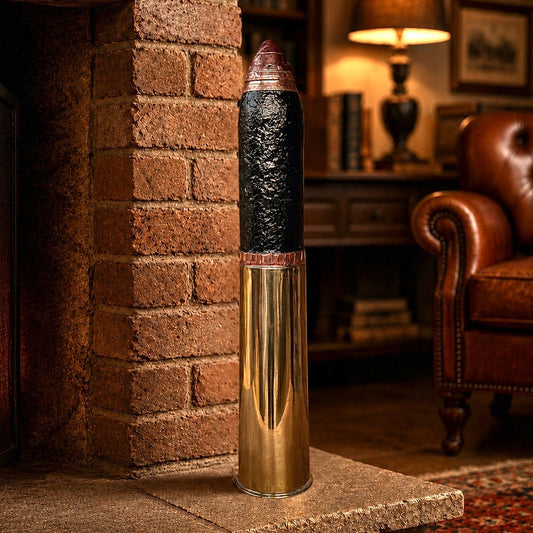 A WW1 18 pounder standing on a stone hearth in a cozy living room beside a brick fireplace. The object has a shiny gold lower section, a textured black middle section, and a dark metallic top.