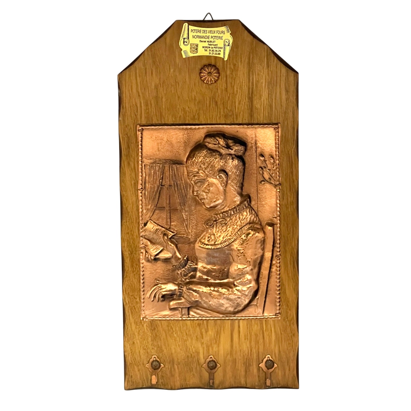 A wooden wall hanging plaque featuring a raised relief carving of a seated woman in traditional dress, with three metal hooks at the bottom and a small gold-colored hanging tag at the top.