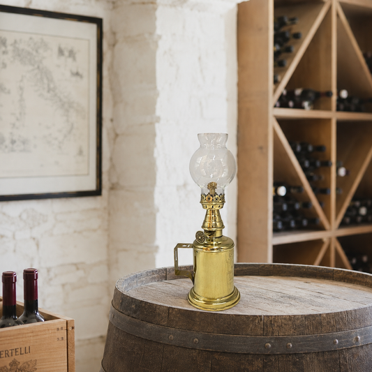 Vintage small brass oil lamp on a wooden barrel with wine bottles in the background
