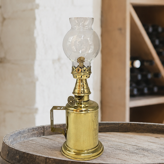 Vintage brass oil lamp with glass shade on a wooden barrel in a rustic setting