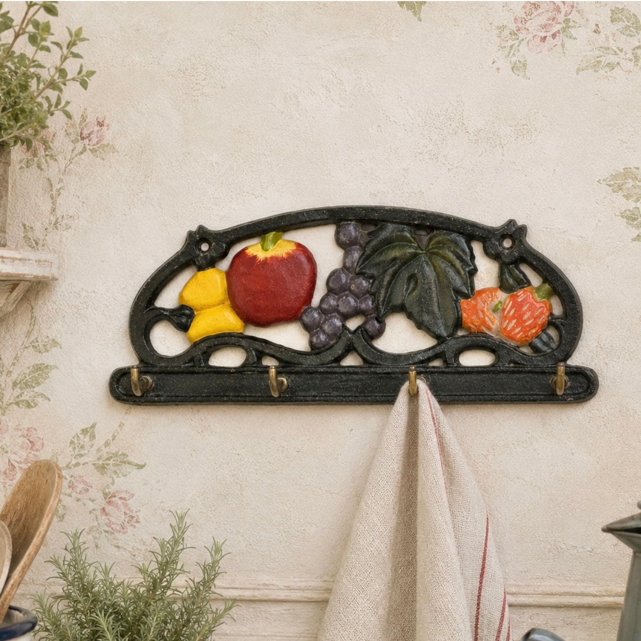 A decorative black metal fruit wall hook rack mounted on a floral wallpapered wall, holding a beige towel.