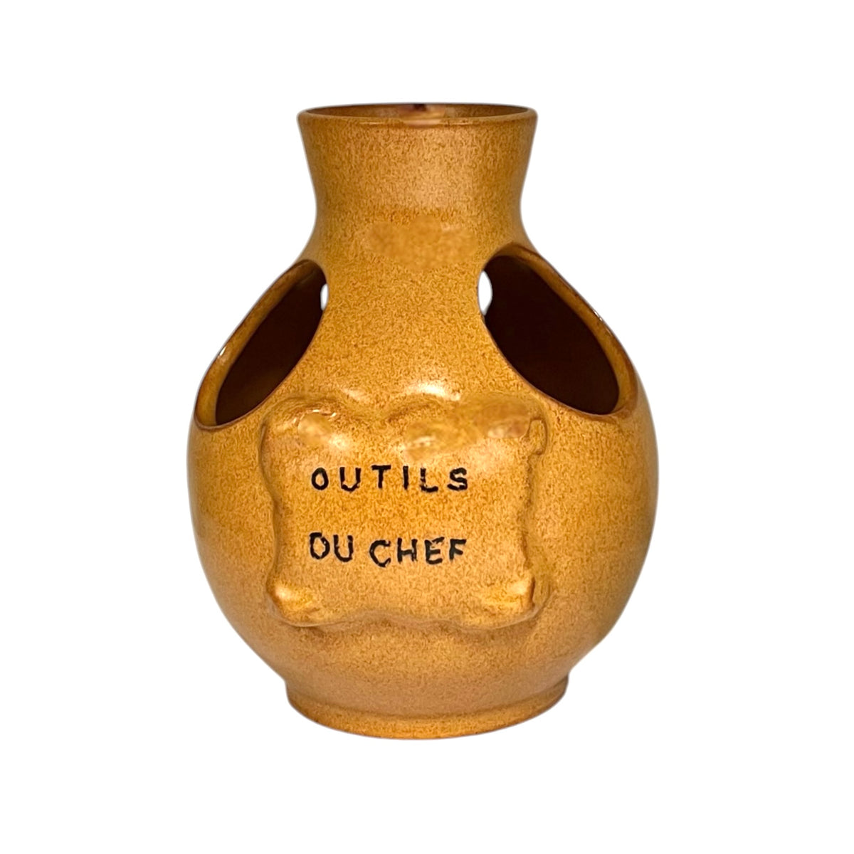 Vintage French ceramic kitchen utensil holder with a honey-brown mottled glaze, rounded body and two large angled side openings. Raised front plaque inscribed Outils du Chef, meaning Chef's Tools. Traditional rustic French country kitchen pottery measuring 18.5 cm high, sourced from a French brocante and shown on a plain white background 