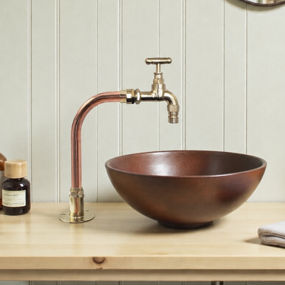 Copper sink with bronze faucet on a wooden countertop against a light wooden panel wall.
