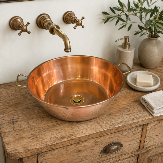 Copper sink on a wooden cabinet with brass fixtures and a plant in the background.