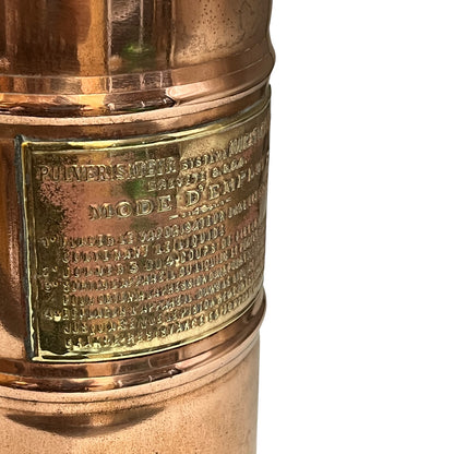 Close-up of a brass or copper lamp with engraved text on a white background